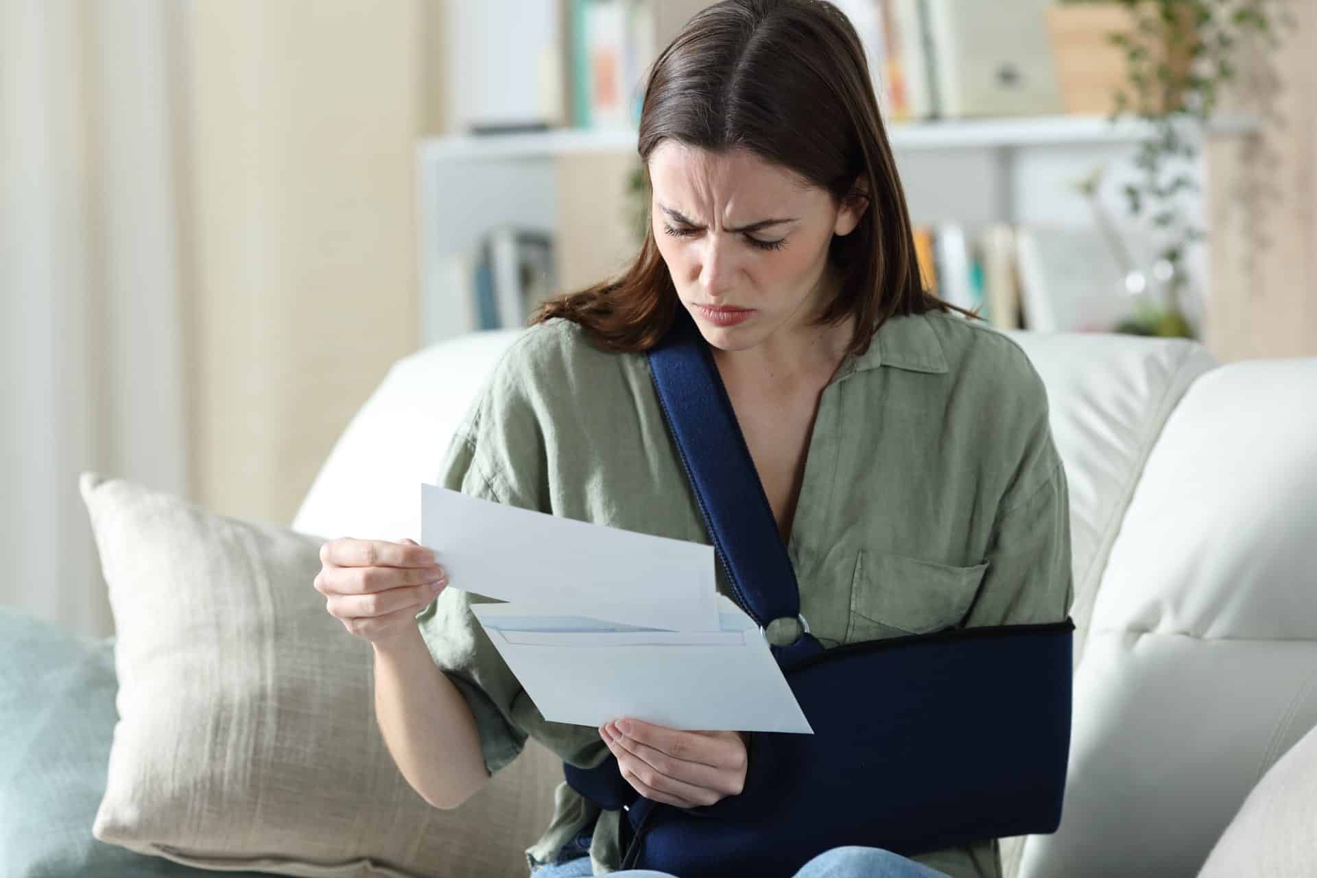 Woman sitting on couch holding paperwork in an arm sling