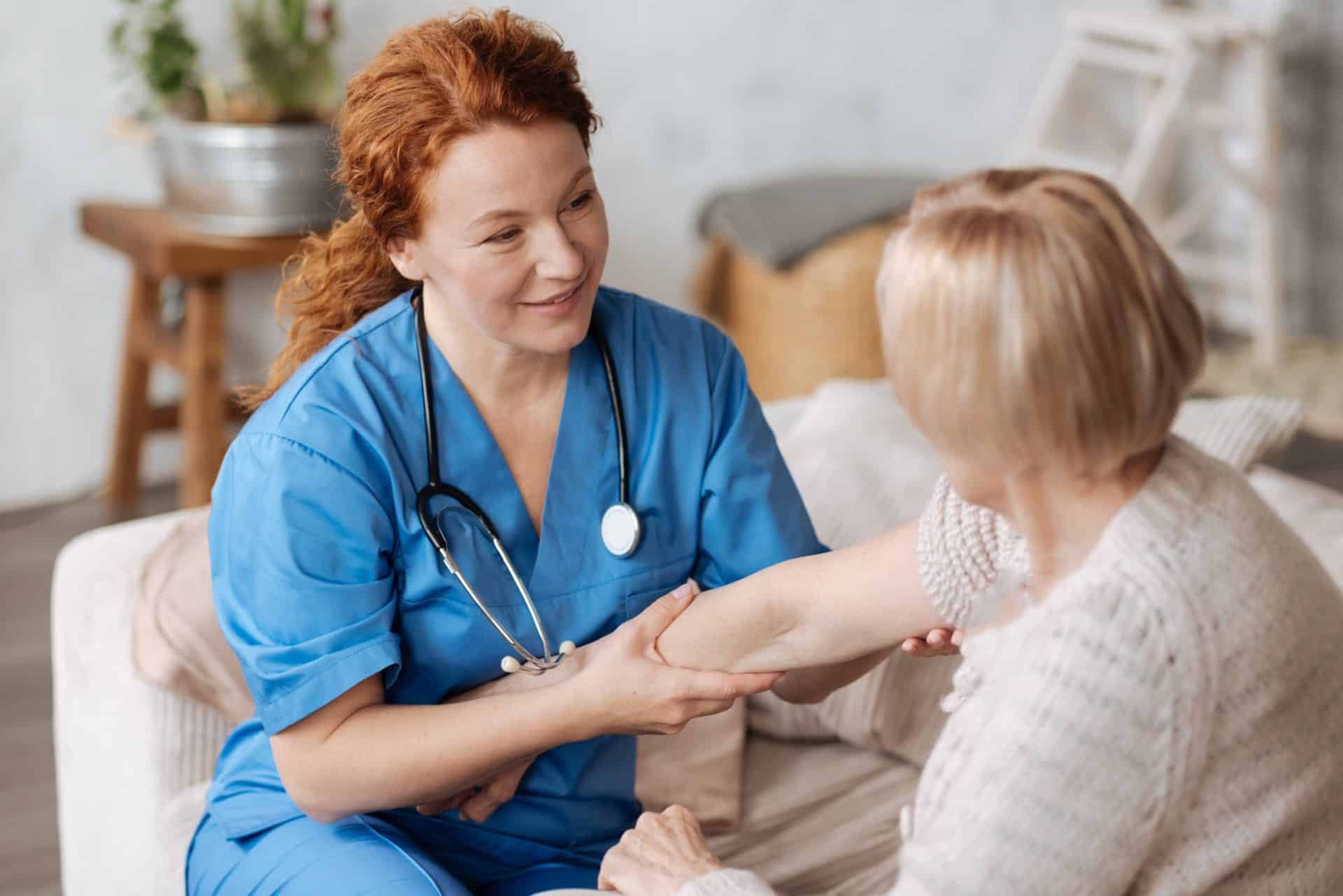 A woman in blue scrubs with a stethoscope around her neck examining another woman