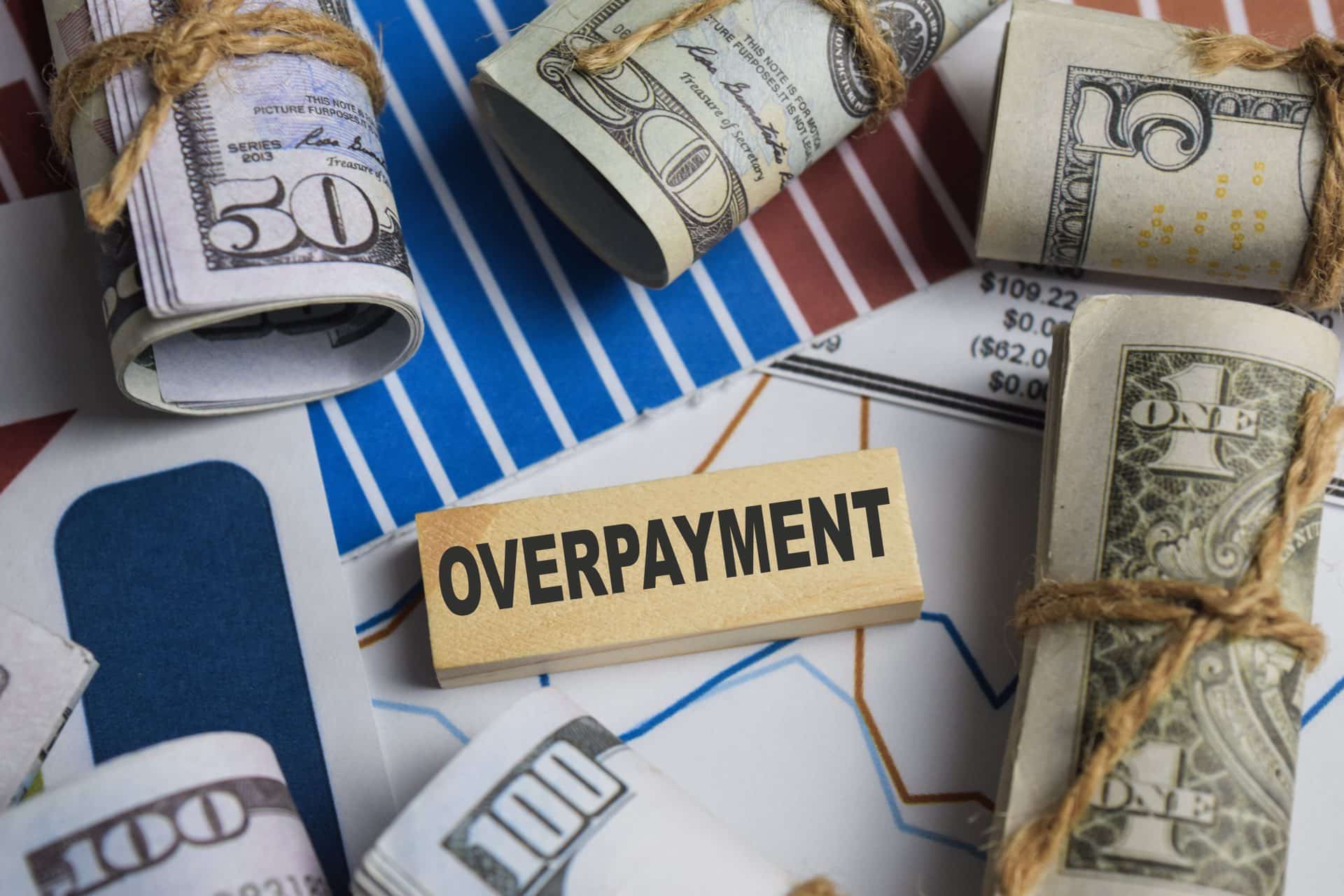 A wooden block that says overpayment in the middle of rolled up money